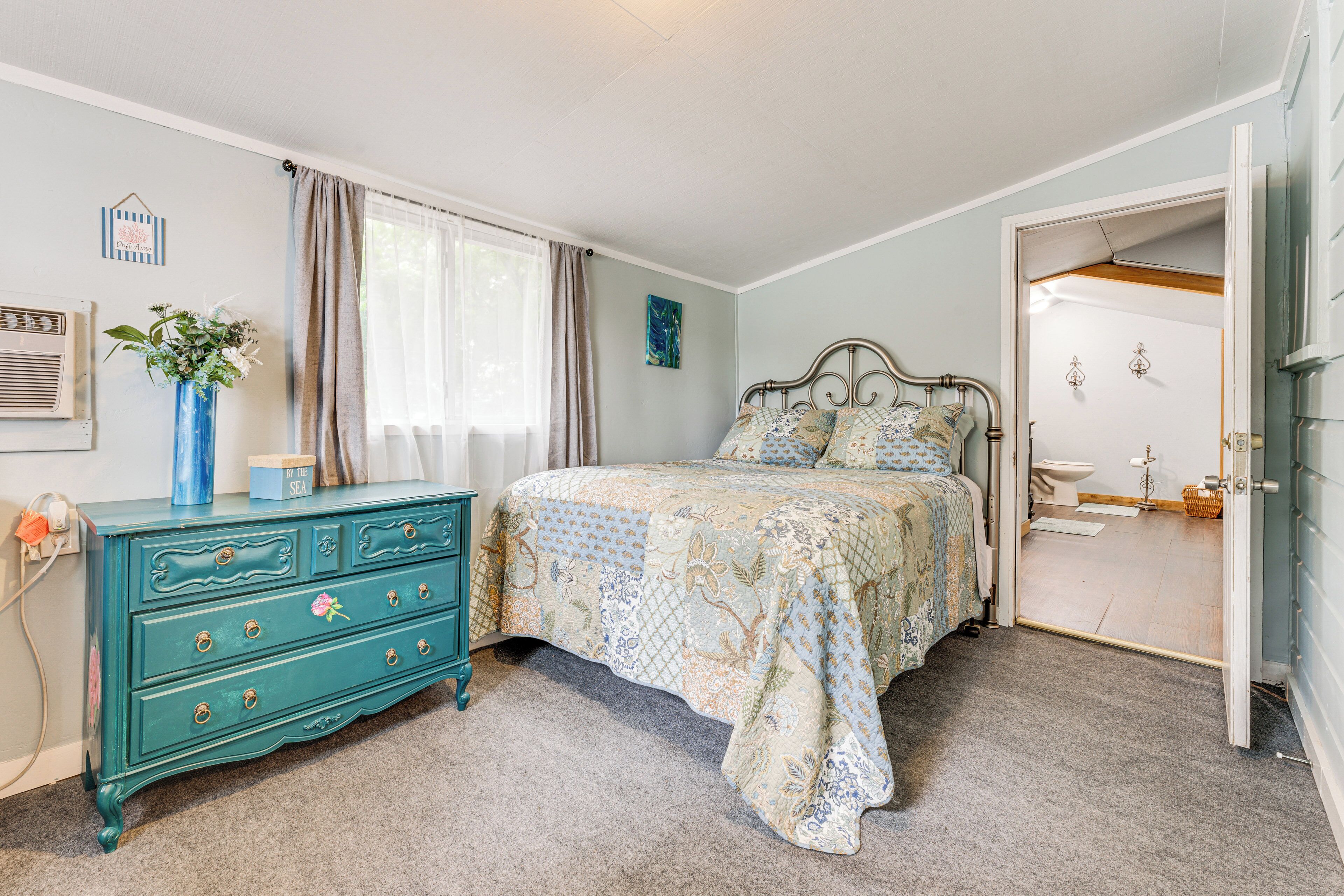 A bedroom with a bed, dresser, and a bathroom visible through an open door.