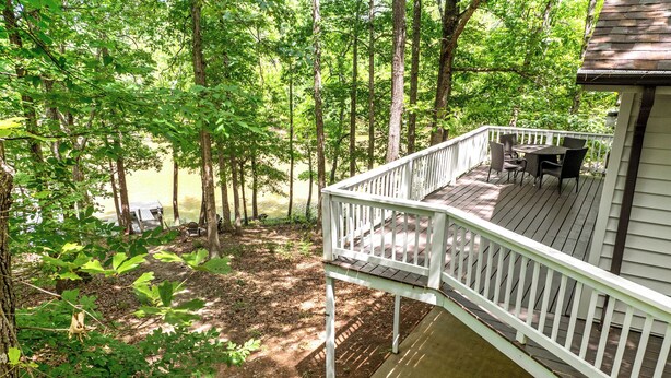 A wooden deck with outdoor furniture, surrounded by trees and a body of water. - Charming waterfront retreat on Buggs Island/Kerr Lake—perfect lakeside living! (Clarksville)