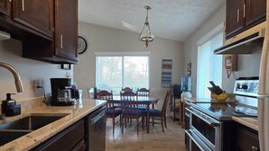A kitchen with dark wood cabinets, a granite countertop, a dining table with chairs, a hanging light fixture, and a large window with blinds. - Charming waterfront retreat on Buggs Island/Kerr Lake—perfect lakeside living! (Clarksville)