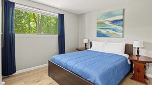 A bedroom with a large bed, two bedside tables with lamps, a window with curtains, and a painting on the wall. - Charming waterfront retreat on Buggs Island/Kerr Lake—perfect lakeside living! (Clarksville)