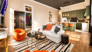 A modern living room with a sofa, coffee table, and orange chairs. There is a kitchen with green cabinets and a dining area with a table and chairs. - 8 Bed 6 Bath Waterfront Views Bourbon Trail w/Firepit HotTub Dome Luxe Amenities (Jeffersonville)