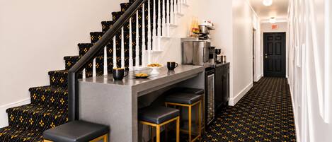 Una escalera con alfombra de estampado negro y amarillo, una zona de bar con taburetes y una cocina con electrodomésticos.