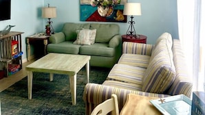 Un salon avec un canapé vert, un canapé à rayures, une table basse en bois et un ventilateur de plafond.