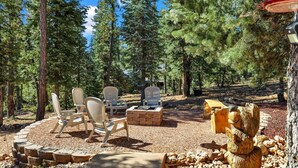 A forested outdoor seating area with chairs and a fire pit.