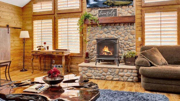 A cozy cabin interior with a stone fireplace, wooden walls, a comfortable couch, and a desk with a lamp.