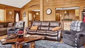 A cozy cabin interior with a leather sofa, armchairs, and a rustic wooden table.