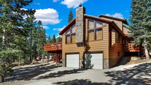A log cabin with a stone chimney, large windows, and a covered deck.