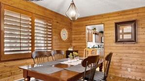 A wooden dining room with a large table, chairs, and a chandelier.