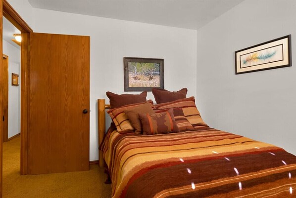 Ein Schlafzimmer mit Holztür, einem Bett mit gestreifter Bettwäsche und zwei gerahmten Bildern an der Wand.