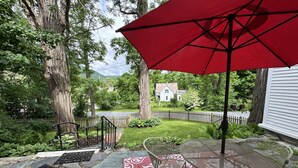 A patio with stone flooring, metal chairs, and a red umbrella. - Your next peaceful getaway in Arlington VT! (Arlington)