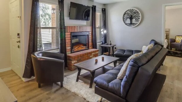 A living room with a fireplace, leather sofa, and a TV mounted on the wall. - 2BR Condo with patio, Heated Pool, Spa & Gym Access (Phoenix)
