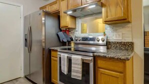 A compact kitchen with wooden cabinets, a stainless steel refrigerator, a stove, and a microwave. - 2BR Condo with patio, Heated Pool, Spa & Gym Access (Phoenix)