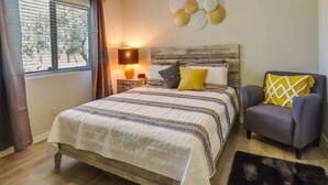 A bedroom with a large bed, a nightstand, a lamp, a chair, and a decorative wall piece. - 2BR Condo with patio, Heated Pool, Spa & Gym Access (Phoenix)