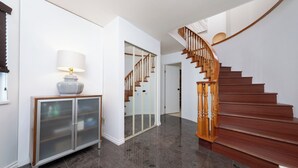 A modern interior with a polished wooden staircase, a glass cabinet, and a lamp.