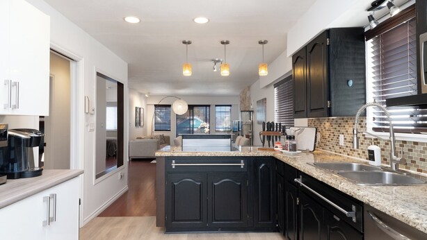 A modern kitchen with granite countertops, black cabinetry, and stainless steel appliances.