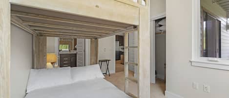 A bunk bed room with a wooden ceiling, a desk, and a window.