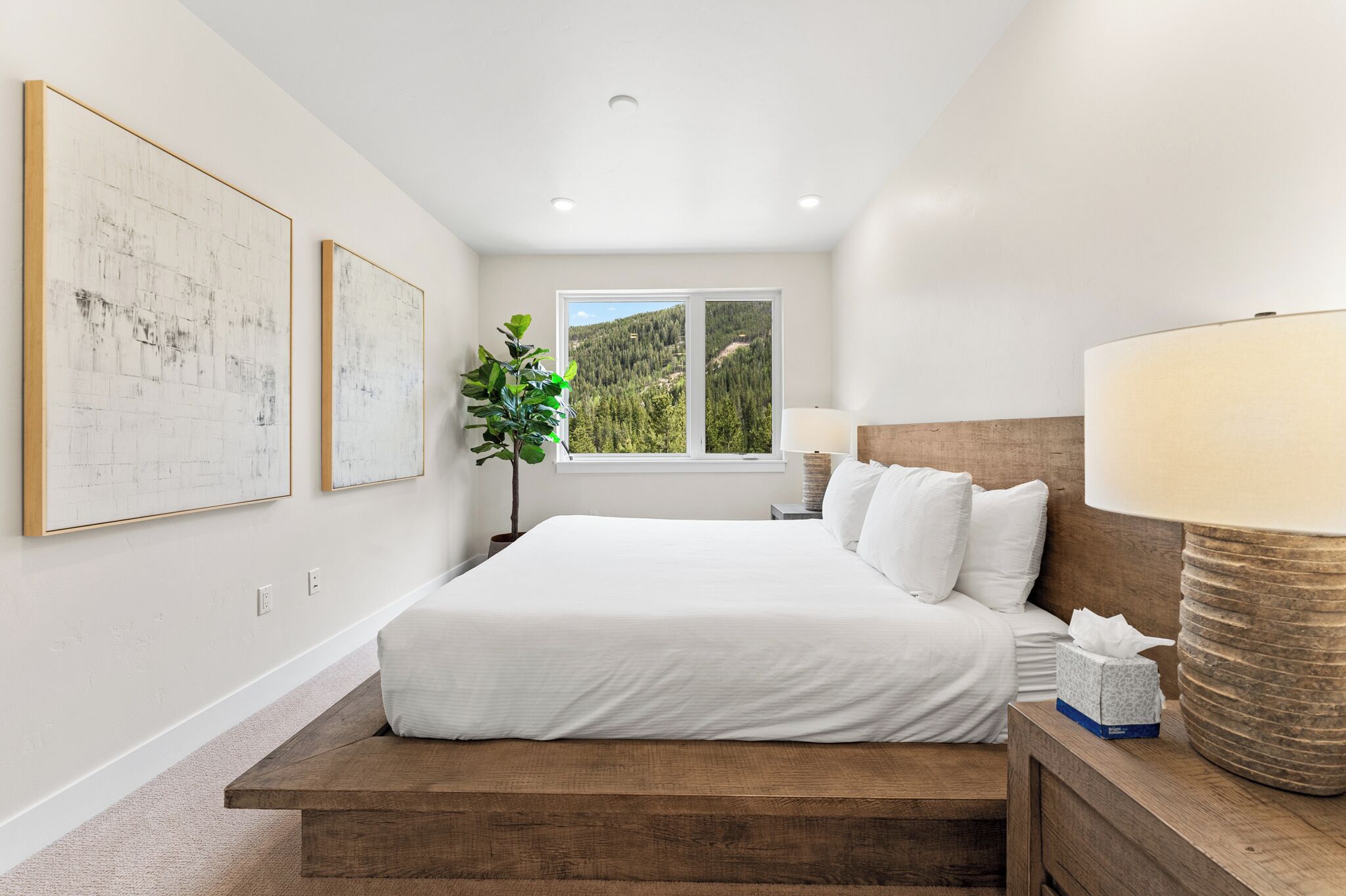 Un dormitorio con una cama grande, una ventana que da a un bosque y dos cuadros en la pared.