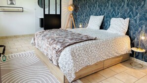 A modern bedroom with a large bed, a dark patterned wall, a round mirror, and a small table with a lamp. - Villa Normande Piscine Intérieur et Jeux / Proche Honfleur et Deauville (Selles)