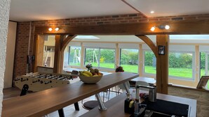 A modern kitchen with a foosball table, a bowl of fruit, and a large window overlooking a garden. - Villa Normande Piscine Intérieur et Jeux / Proche Honfleur et Deauville (Selles)