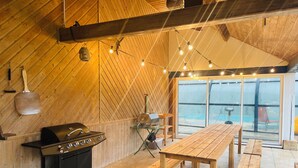 A wooden interior with a grill, wooden tables, and string lights. - Villa Normande Piscine Intérieur et Jeux / Proche Honfleur et Deauville (Selles)