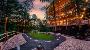 Un bâtiment en bois à plusieurs niveaux, décoré de guirlandes lumineuses, entouré d’arbres et bordé d’un chemin de gravier.