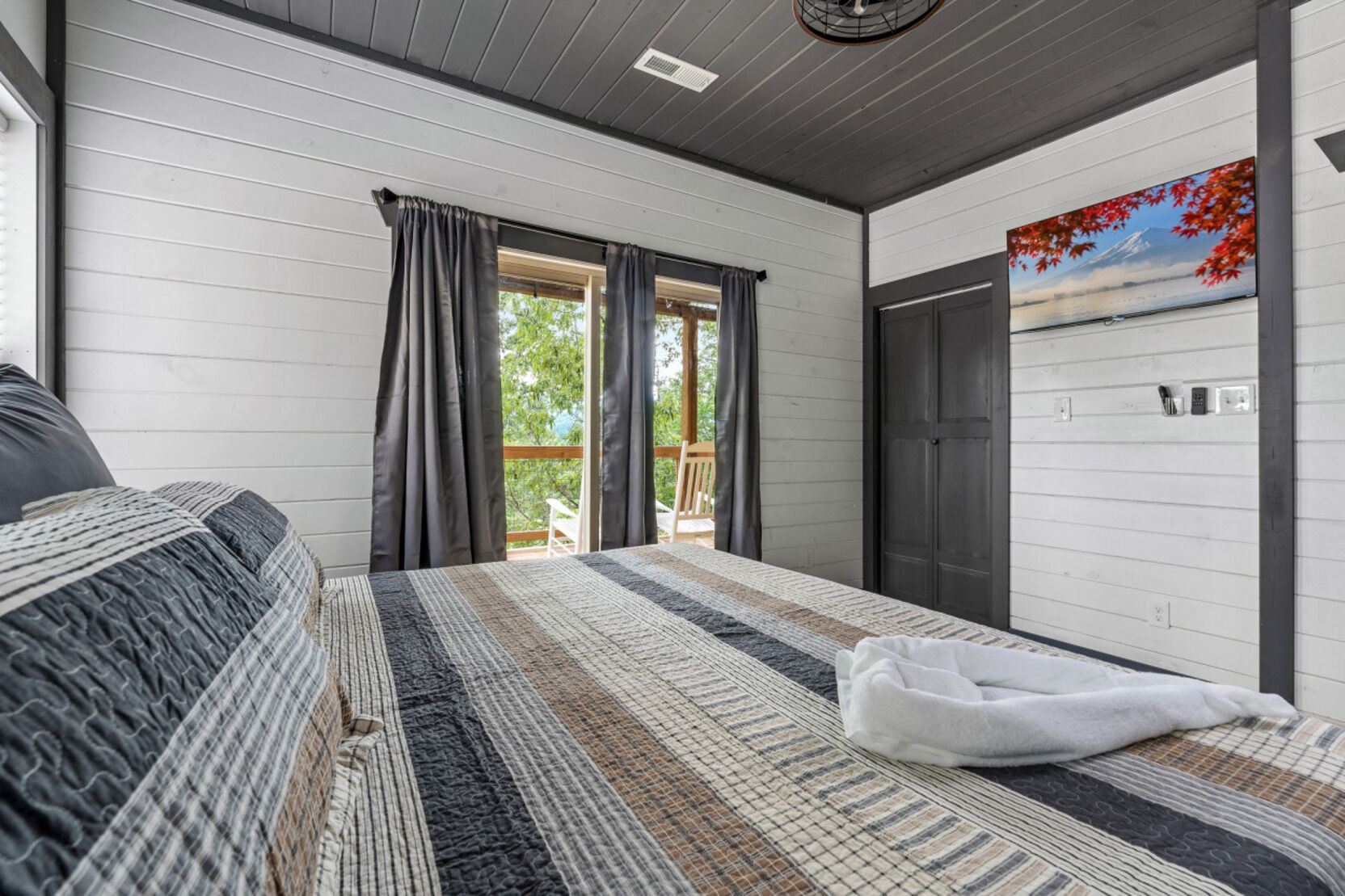 A bedroom with a large bed, a view of the outdoors through a window, and a painting on the wall.