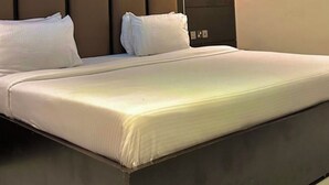 A modern hotel room with a large bed, a headboard with vertical panels, and a wall-mounted light. - Rosmohr Vintage (Uyo)