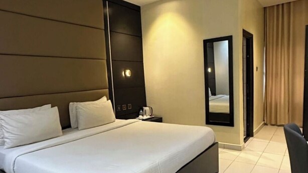 A modern hotel room with a large bed, a bedside table, a chair, and a mirror. - Rosmohr Vintage (Uyo)