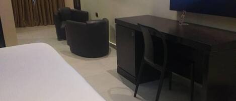 A hotel room with a large bed, a desk, a chair, and a television on the wall.