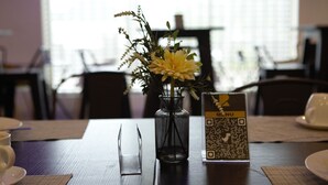 A dining table with a vase of flowers, a QR code menu, and a cup. - Rosmohr Vintage (Uyo)