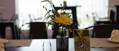 Une table à manger ornée d’un vase de fleurs, d’un menu accessible via un code QR et d’une tasse.