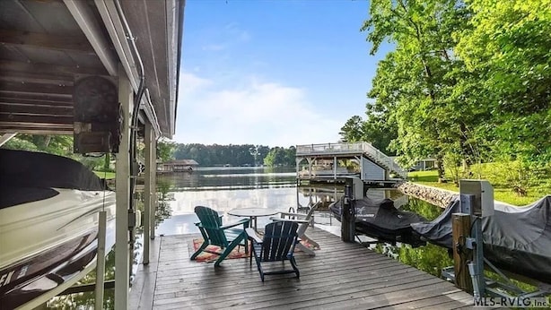Terraza de madera con dos sillas y una mesa, con vista a un lago tranquilo.
