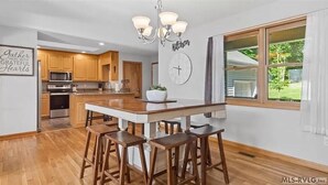 Una cocina moderna con armarios de madera, una isla central con taburetes, una araña y un reloj en la pared.