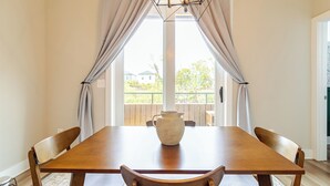 A dining area with a wooden table, six chairs, a vase, and a view through large windows. - Southside Retreat with Coffee Bar & Garage (Chattanooga)