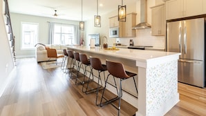 A modern kitchen with a large island, bar stools, stainless steel appliances, and pendant lighting. - Southside Retreat with Coffee Bar & Garage (Chattanooga)