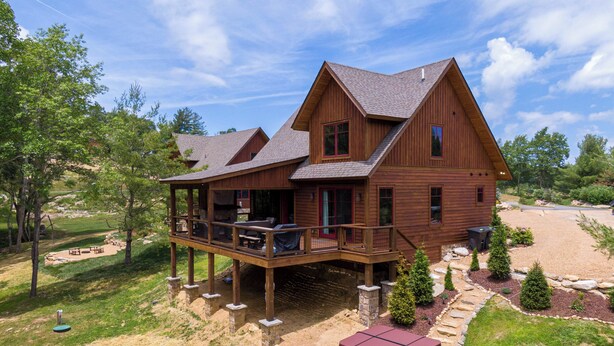 Een houten chalet met twee verdiepingen, voorzien van een balkon en terras, gelegen in een aangelegde tuin met bomen.
