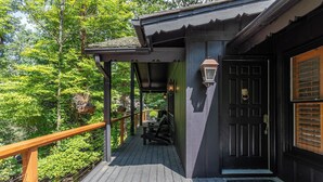 A wooden deck with a black door and a 'hello' mat, surrounded by lush greenery. - Elk Watch at Hound Ears (Boone)