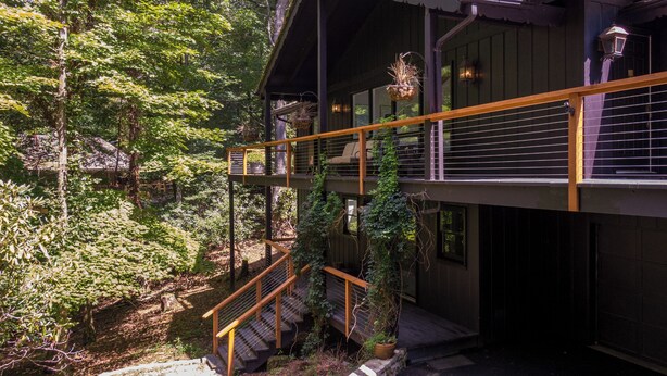 A multi-level wooden building with outdoor stairs, surrounded by dense foliage. - Elk Watch at Hound Ears (Boone)