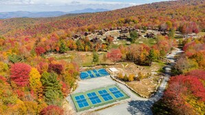 An aerial view of a resort with multiple buildings, a tennis court, and a river. - Three Little Bears at Eagles Nest (Banner Elk)