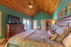 A bedroom with a wooden ceiling, a bed with patterned bedding, a dresser, and a television on top. - Stags Leap at Yonahlossee (Boone)