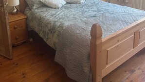 Una cama de madera con una colcha estampada, dos mesitas de noche con lámparas y un radiador.