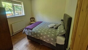 Un dormitorio con cama, un radiador, una ventana y una silla.