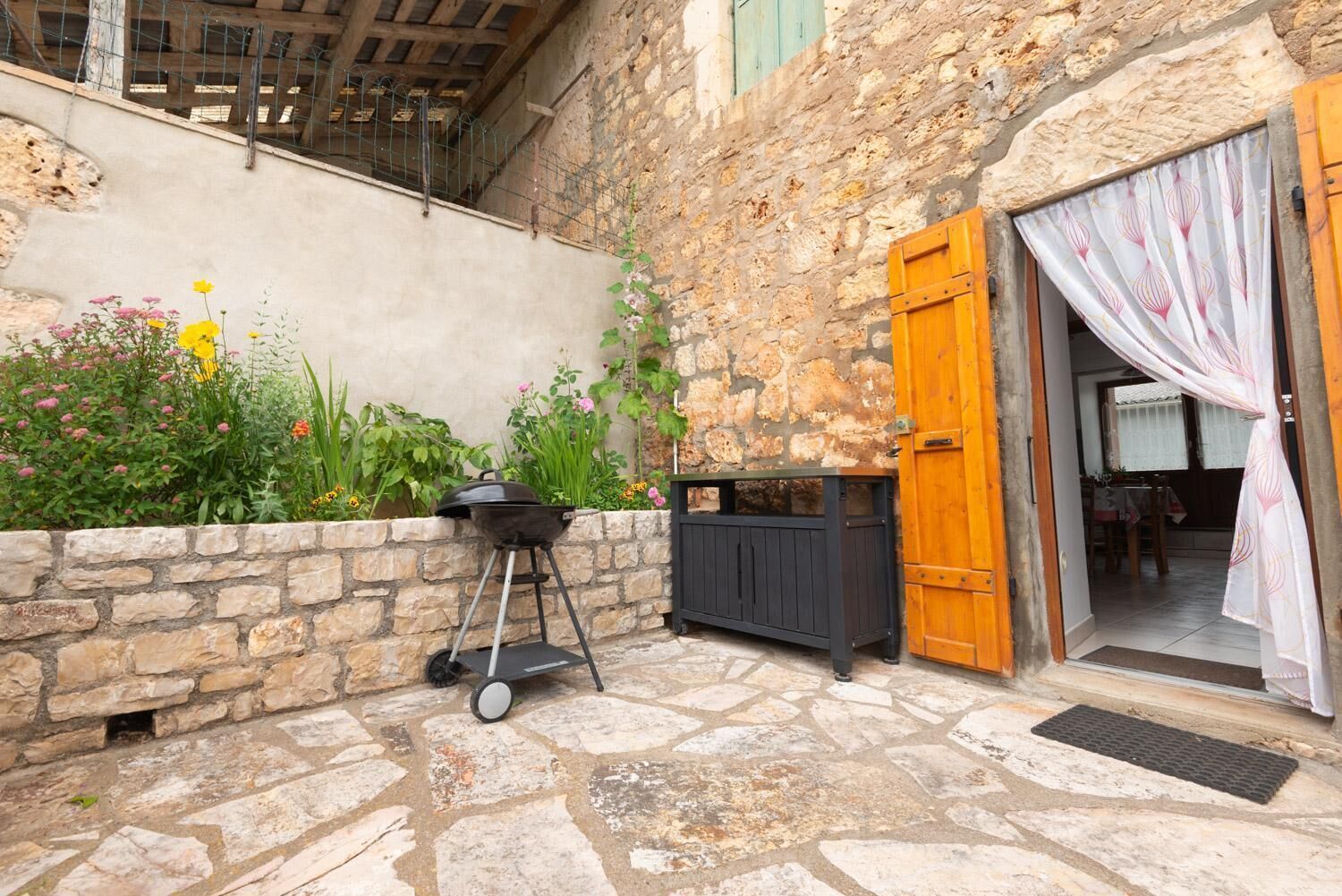 Une cour pavée de pierres, avec un barbecue, une porte en bois et une petite table.