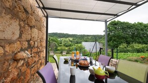 Un espace de restauration en plein air avec un mur en pierre, une table dressée avec des assiettes, des verres et une théière, et une vue sur un paysage verdoyant.