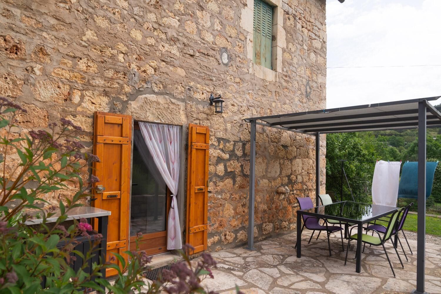 Un edificio de piedra con puerta de madera y un espacio exterior cubierto con sillas y una mesa.