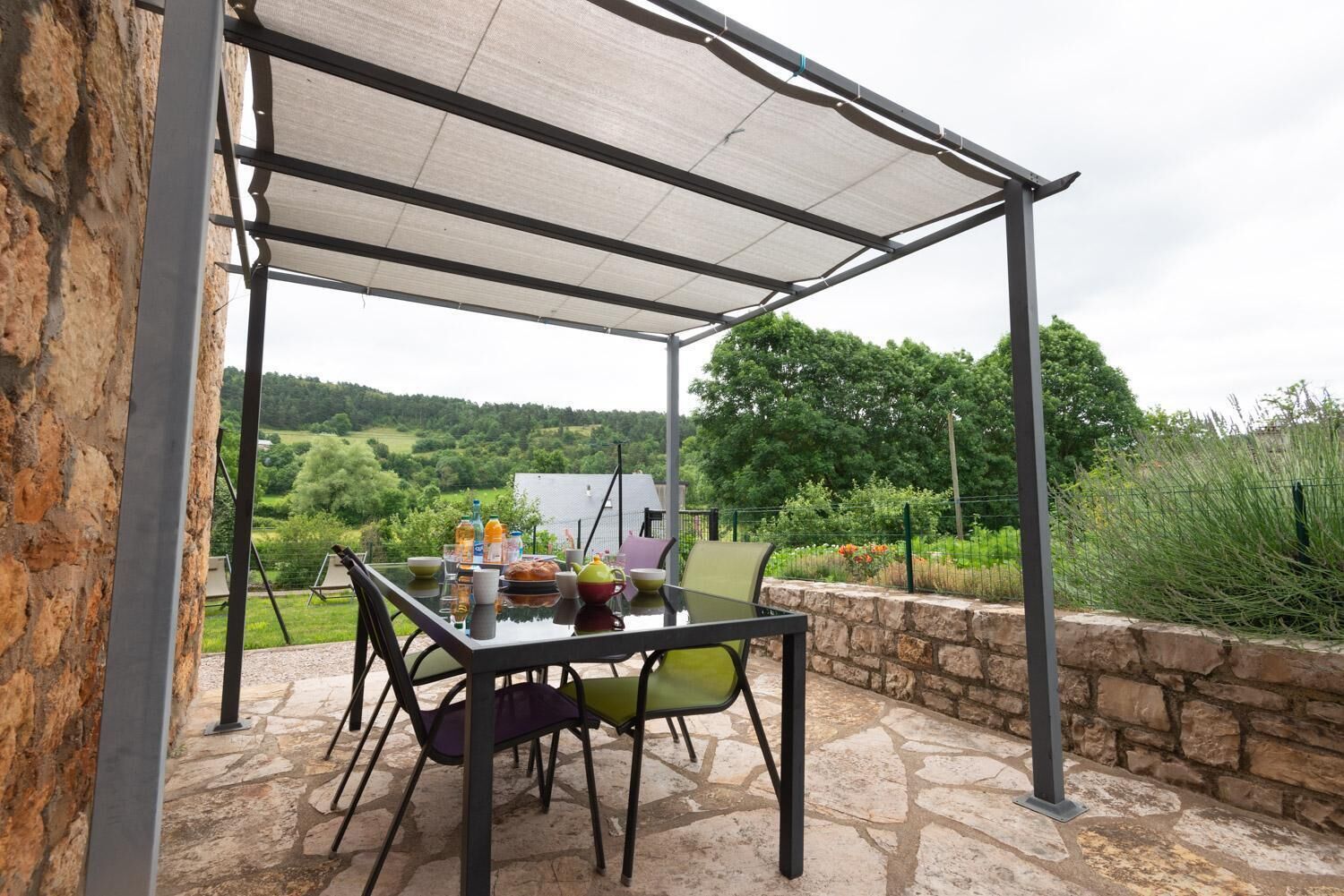 Une terrasse extérieure avec une table dressée pour le repas, entourée de murs en pierre et offrant une vue sur un paysage verdoyant.