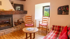 A cozy living room with a fireplace, two wooden chairs, a round wooden table, and a plaid sofa. - To the summits of the Gorges du Tarn (LAVAL DU TARN)