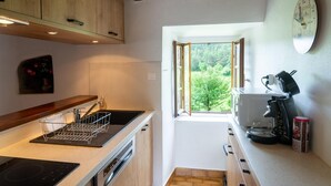 A compact kitchen with wooden cabinets, a built-in oven, a coffee machine, and a window providing a view of greenery outside. - To the summits of the Gorges du Tarn (LAVAL DU TARN)