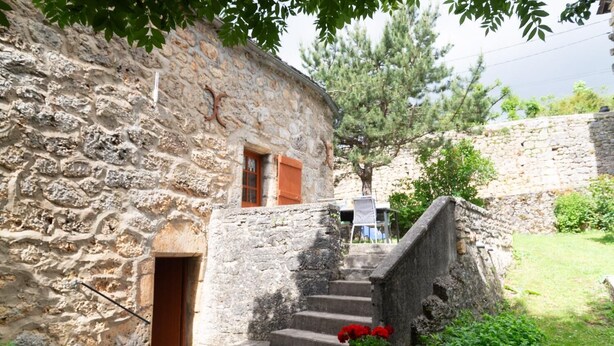 A stone building with a staircase leading to a door, surrounded by greenery and trees. - To the summits of the Gorges du Tarn (LAVAL DU TARN)