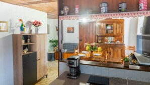 A cozy kitchen with wooden cabinets, a coffee maker, and a dining area with a table set for two. - L'Oustal de Julie 3 people (LAVAL DU TARN)
